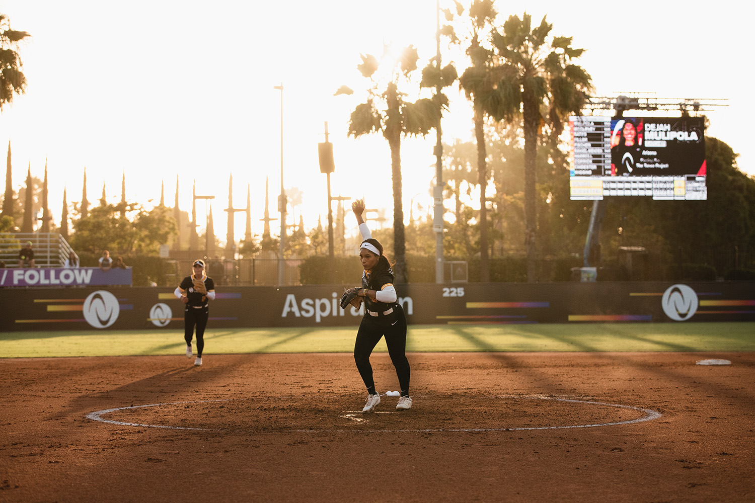 Aleshia Ocasio pitches in front of a backdrop of palm trees and sunlight.