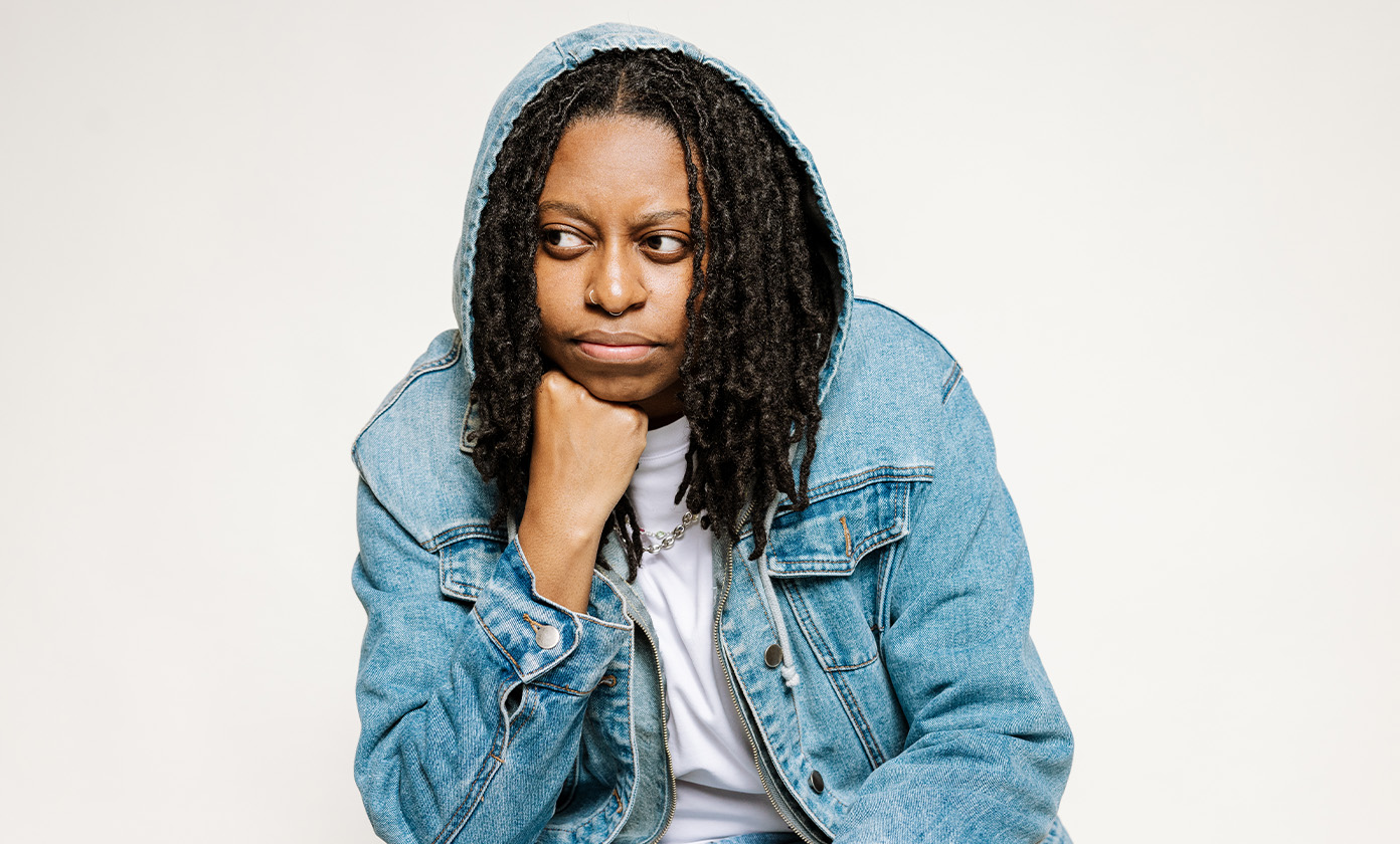 Daisha McBride in jean jacket propping her head up with her hand and looking off to the side