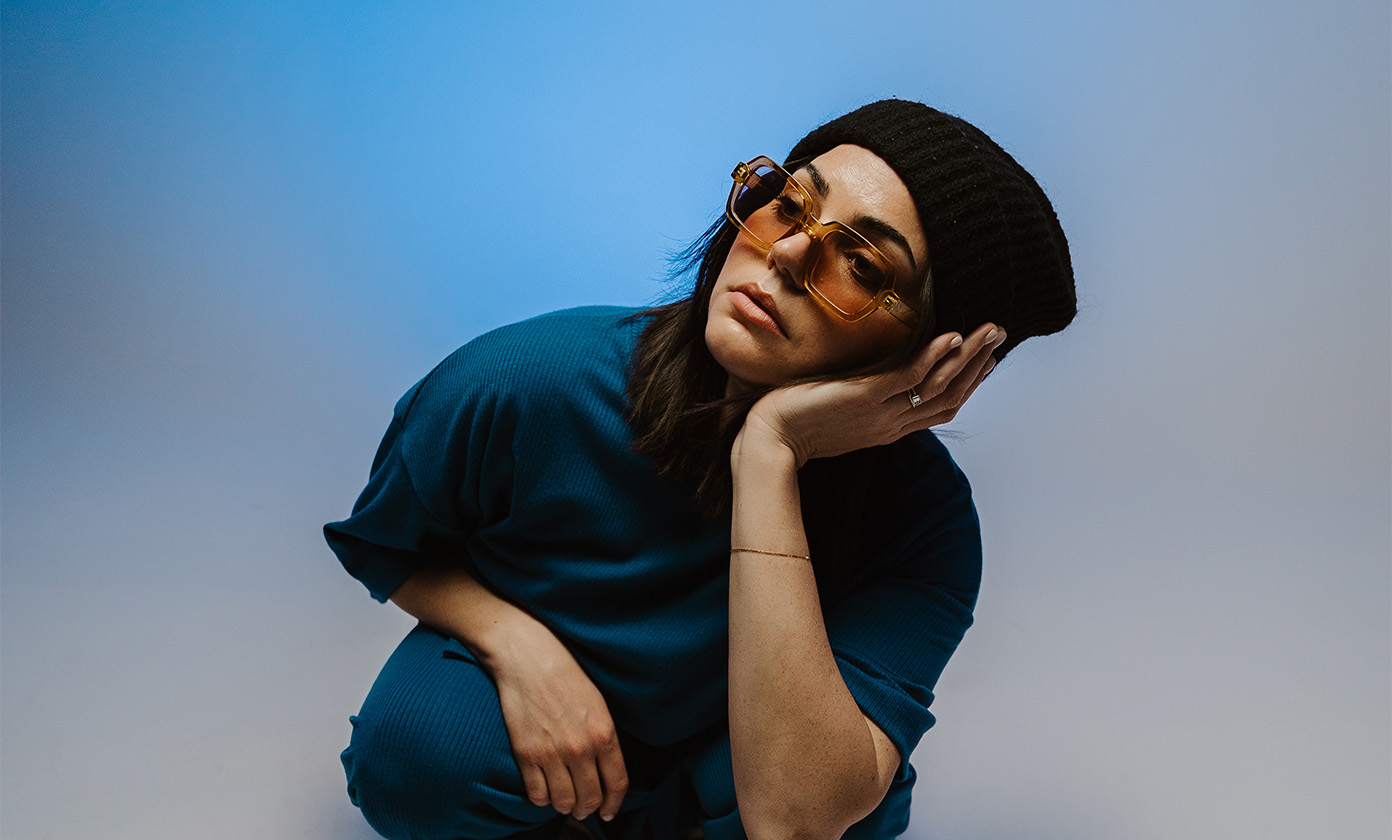 Julie Melucci wearing black hat and orange shaded glasses holding her head up